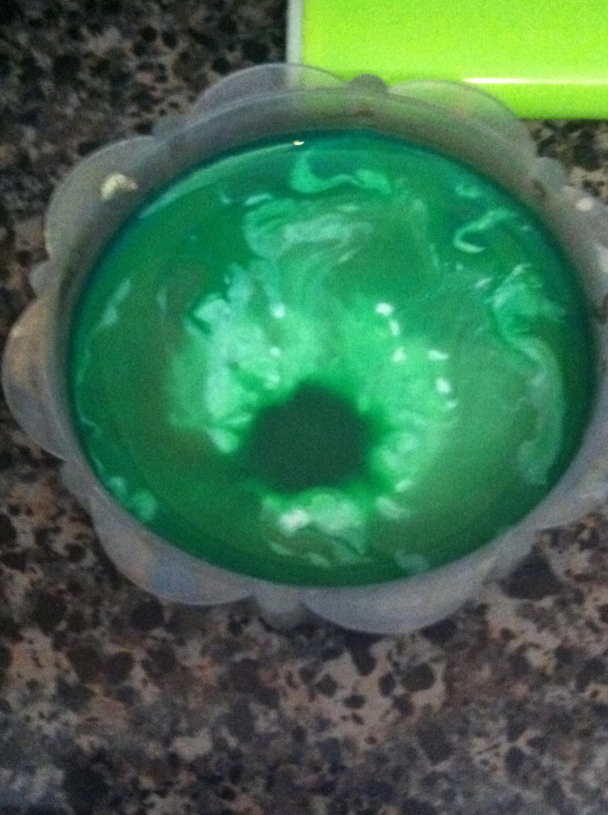 A dish, semi filled with water, with 6 drops of green paint, the glow paint, and then an additional green drop