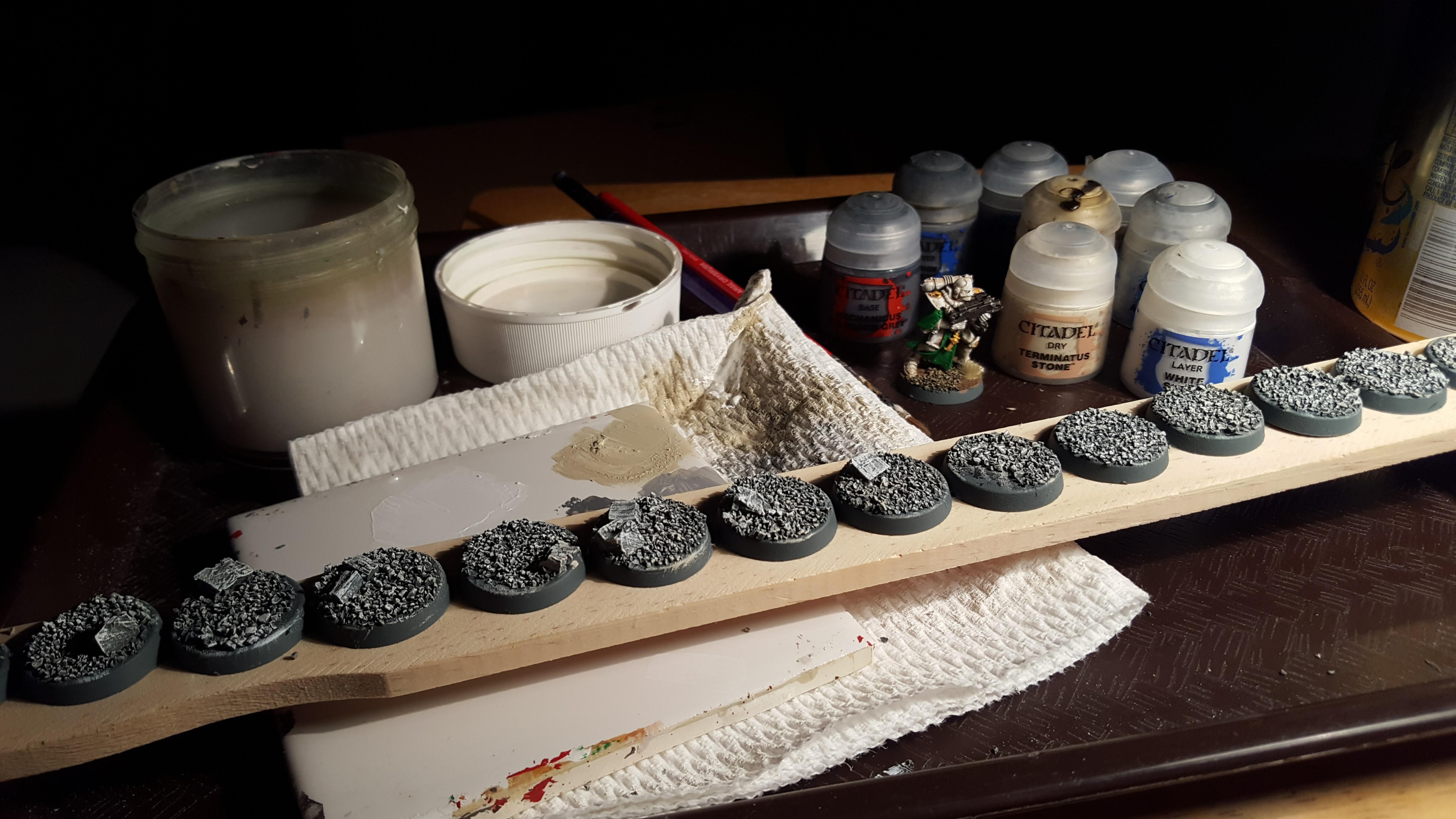 Mass-producing bases on a paint stirrer: PVA glue, cork and gravel, Mechanicus Grey spray, Terminatus Stone and White Scar drybrush, Agrax Earth wash