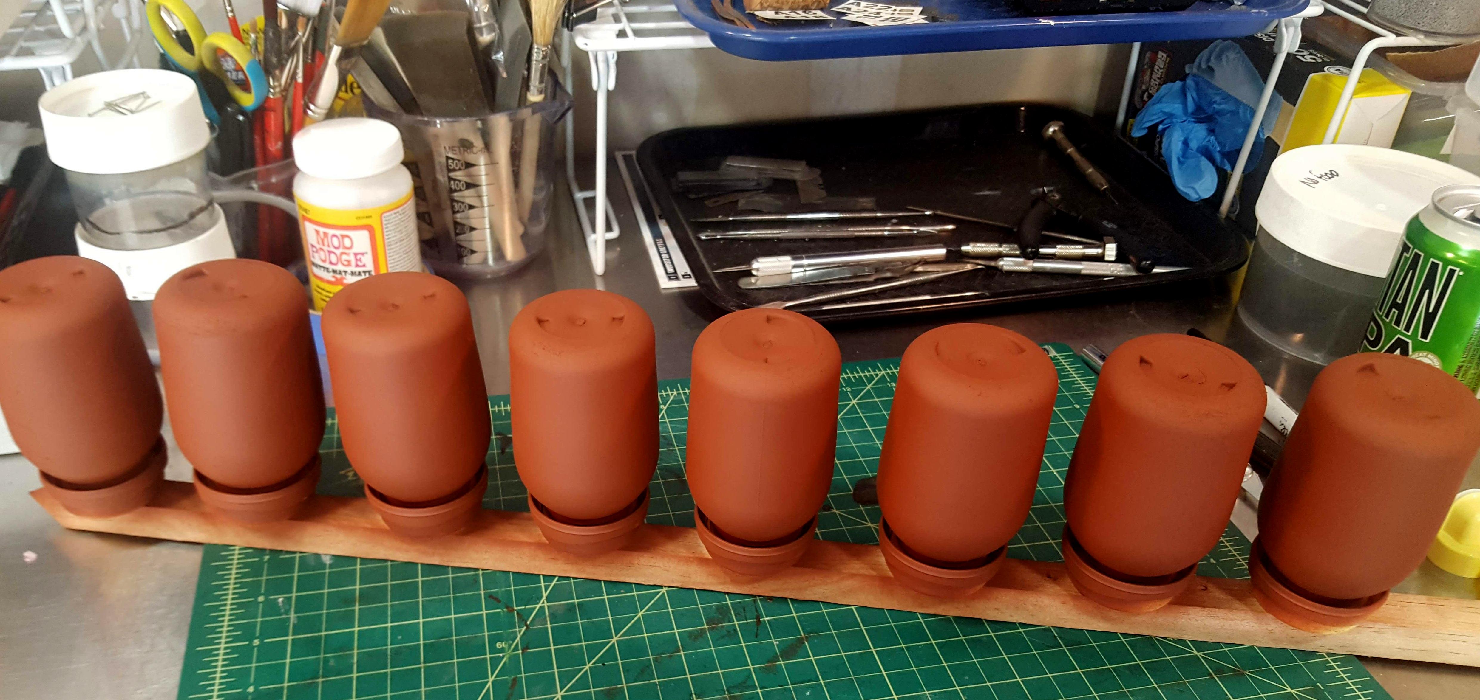 Eight repurposed milk bottles undercoated with red-brown primer